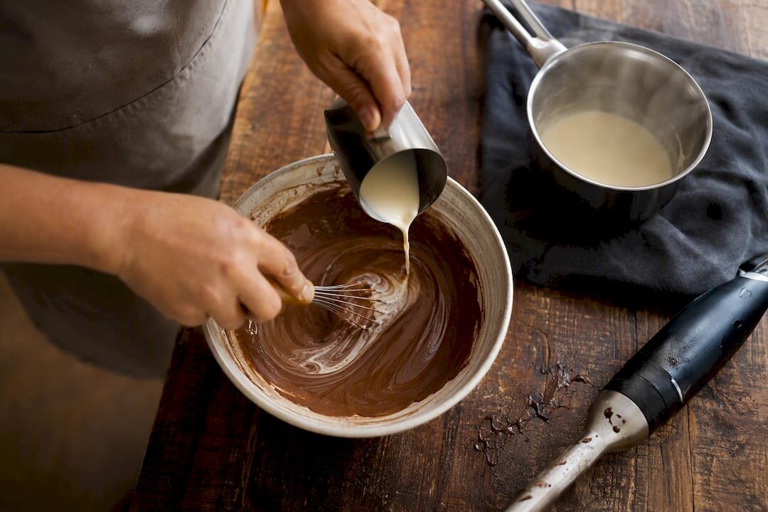 Handen die gebroken ganache met room en een garde herstellen
