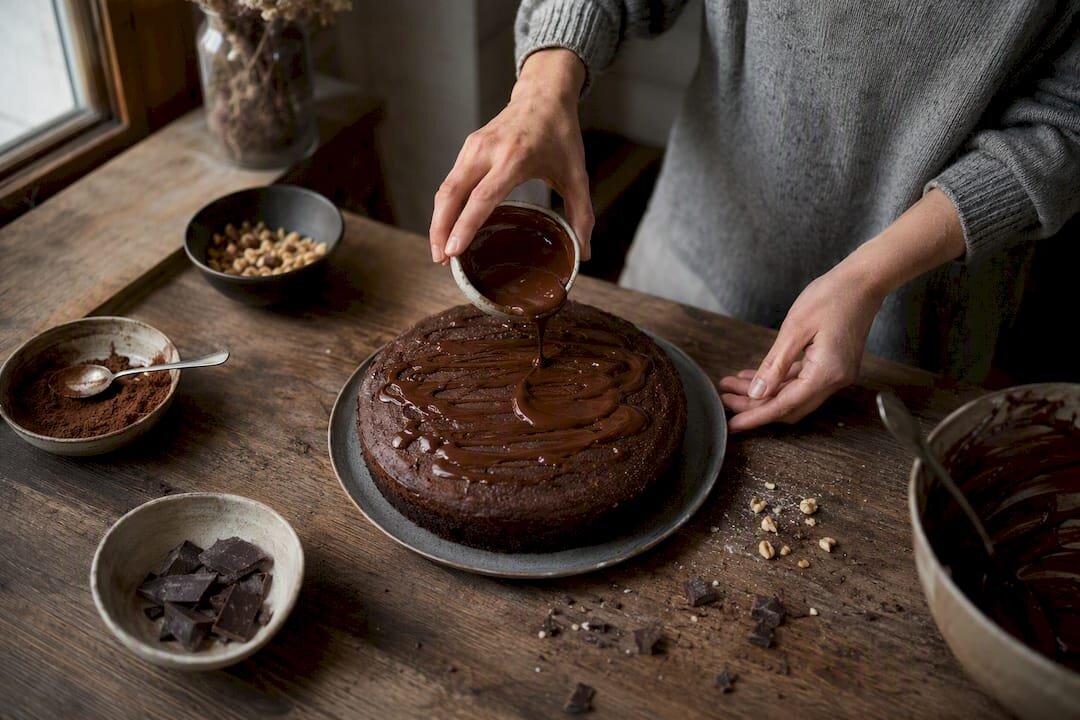 Handen die een chocoladetaart afwerken met cacaopoeder